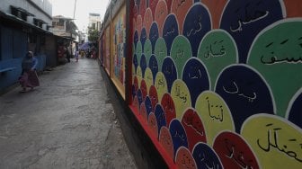 Warga melihat mural edukasi pada tembok di kawasan Pademangan Timur, Jakarta Utara, Minggu (17/11). [Suara.com/Angga Budhiyanto]