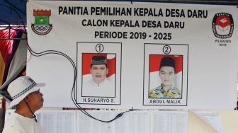 Seorang warga mengamati foto calon kepala desa untuk pemilihan Kepala Desa yang calonnya merupakan anak dan bapak yakni Suharyo (bapak) dan Abdul Malik (anak) di Desa Daru, Kabupaten Tangerang, Banten, Minggu (1/12).  [ANTARA FOTO/Muhammad Iqbal]
