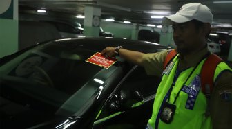 Petugas Samsat Jakarta Pusat menempelkan stiker 'Objek Pajak' pada mobil mewah saat razia supervisi pencegahan pajak mobil mewah di Apartemen Pavilion, Jakarta Pusat, Senin (9/12). [Suara.com/Angga Budhiyanto]