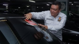 Petugas Samsat Jakarta Pusat menempelkan stiker 'Objek Pajak' pada mobil mewah saat razia supervisi pencegahan pajak mobil mewah di Apartemen Pavilion, Jakarta Pusat, Senin (9/12). [Suara.com/Angga Budhiyanto]