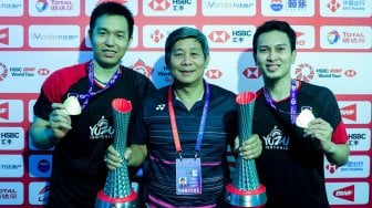 Ganda putra Indonesia Hendra Setiawan (kiri) dan Mohammad Ahsan (kanan) bersama pelatihnya Herry Iman Pierngadi menunjukan medali dan piala usai mengalahkan ganda putra Jepang Hiroyuki Endo dan Yuta Watanabe pada final BWF World Tour Finals 2019 di Tianhe Gymnasium, Guangzhou, China, Minggu (15/12). [ANTARA FOTO/Bimo - Humas PBSI]