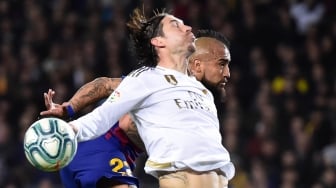 Bek Real Madrid Sergio Ramos dan pemain tengah Barcelona Arturo Vidal melompat untuk merebut bola selama pertandingan sepak bola Liga Spanyol "El Clasico" antara Barcelona melawan Real Madrid di Camp, Barcelona, Spanyol, Kamis (18/12) dini hari WIB.  [JOSE JORDAN / AFP]
