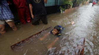 Seorang anak bermain di jalan yang terendam banjir di kawasan Jatipadang, Pasar Minggu, Jakarta Selatan, Rabu (1/1). [Suara.com/Angga Budhiyanto]