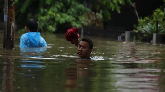 Warga melintasi jalan yang terendam banjir di kawasan Kebon Pala, Jakarta Timur, Rabu (1/1). [Suara.com/Angga Budhiyanto]