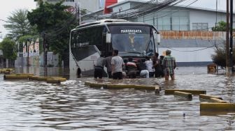 Warga melintasi jalanan yang terendam banjir di Jalan Daan Mogot, Jakarta Barat, Kamis (2/1). [Suara.com/Angga Budhiyanto]