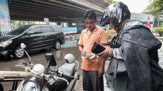 Penumpang yang sedang membayar jasa ojek gerobak setelah menyeberangi Persimpangan Puri Kembangan, Kembangan Pasar Minggu, Jakarta Barat, Jumat (3/1).  [Suara.com/Alfian Winanto]