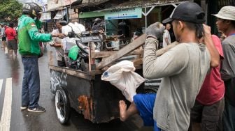 Penumpang ojek gerobak yang sedang berusaha menaikkan motornya untuk menyeberangi Persimpangan Puri Kembangan, Kembangan Pasar Minggu, Jakarta Barat, Jumat (3/1).[Suara.com/Alfian Winanto]