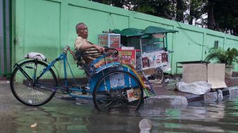 Pengayuh becak menunggu penumpang di jalan yang terendam banjir di Kawasan Teluk Gong, Penjaringan, Jakarta Utara, Sabtu (4/1). [Suara.com/Alfian Winanto]