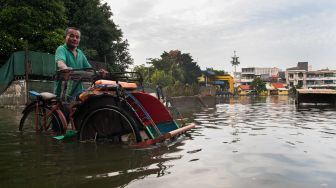 Pengayuh becak menunggu penumpang di jalan yang terendam banjir di Kawasan Teluk Gong, Penjaringan, Jakarta Utara, Sabtu (4/1). [Suara.com/Alfian Winanto]