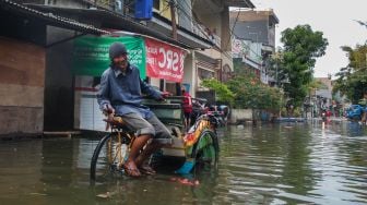 Pengayuh becak menunggu penumpang di jalan yang terendam banjir di Kawasan Teluk Gong, Penjaringan, Jakarta Utara, Sabtu (4/1). [Suara.com/Alfian Winanto]