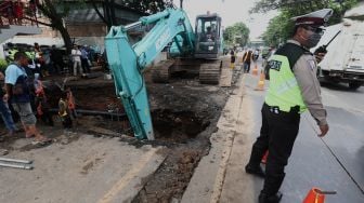 Petugas Kepolisian mengatur lalu lintas di sekitar jalan yang amblas di Jalan Daan Mogot, Kota Tangerang, Banten, Senin (13/1). [Suara.com/Angga Budhiyanto]