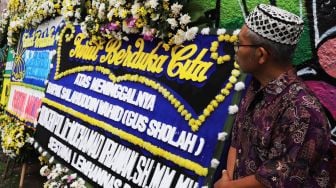 Sejumlah pelayat melintas di depan karangan bunga ucapan belasungkawa atas wafatnya KH Salahuddin Wahid atau Gus Sholah di rumah duka di kawasan Mampang Prapatan, Jakarta, Senin (3/2).[Suara.com/Alfian Winanto]