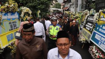 Sejumlah pelayat melintas di depan karangan bunga ucapan belasungkawa atas wafatnya KH Salahuddin Wahid atau Gus Sholah di rumah duka di kawasan Mampang Prapatan, Jakarta, Senin (3/2).[Suara.com/Alfian Winanto]