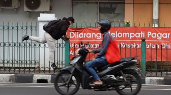 Penumpang KRL menaiki pagar pembatas trotoar di Stasiun Cikini, Jakarta, Rabu (5/2). [Suara.com/Angga Budhiyanto]
