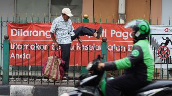 Penumpang KRL menaiki pagar pembatas trotoar di Stasiun Cikini, Jakarta, Rabu (5/2). [Suara.com/Angga Budhiyanto]
