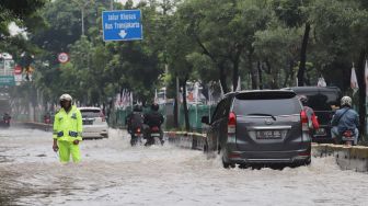 Polisi mengatur lalu-lintas di Jalan Cempaka Putih yang terkena banjir, Jakarta Pusat, Sabtu (08/02).[Suara.com/Alfian Winanto]
