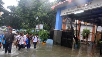 Sejumlah murid melintasi banjir yang menggenangi sekolah SMPN 8, Jakarta, Selasa (25/2). [Suara.com/Oke  Atmaja]
