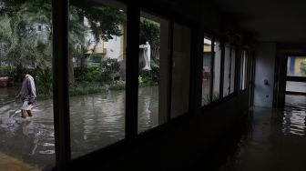 Seorang warga melintas di samping Gereja Santo Kristoforus yang terendam banjir di kawasan Jalan Satria IV, Kelurahan Jelambar, Jakarta Barat, Selasa (25/2). [Suara.com/Angga Budhiyanto]  