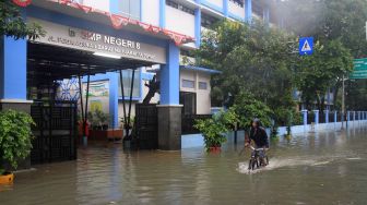 Warga naik sepeda melintasi banjir yang menggenangi sekolah SMPN 8, Jakarta, Selasa (25/2). [Suara.com/Oke  Atmaja]
