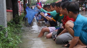 Anak-anak ikut mencari ikan di Jalan Jati Makmur yang tergenang banjir di Bekasi, Jawa Barat, Selasa (25/02). [Suara.com/Alfian Winanto]