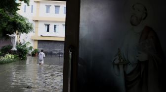 Seorang warga melintas di samping Gereja Santo Kristoforus yang terendam banjir di kawasan Jalan Satria IV, Kelurahan Jelambar, Jakarta Barat, Selasa (25/2). [Suara.com/Angga Budhiyanto]  