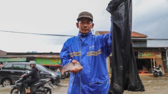 Seorang warga menunjukan ikan hasil tangkapannya dari Jalan Jati Makmur yang tergenang banjir di Bekasi, Jawa Barat, Selasa (25/02).  [Suara.com/Alfian Winanto]