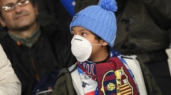 Bocah suporter Napoli mengenakan masker menunggu dimulainya pertandingan Napoli vs Barcelona di Stadion San Paolo, Naples, Italia, Rabu (26/2) dini hari WIB.  [Filippo MONTEFORTE / AFP]