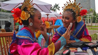 Peserta lomba tari yang saling merias wajahnya sebelum tampil di acara Lomba Tari Betawi di Thamrin 10, Jakarta Pusat, Sabtu (29/02). [Suara.com/Alfian Winanto]