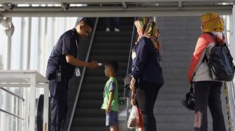 Petugas meriksa suhu tubuh seorang anak kecil calon penumpang sebelum memasuki Stasiun LRT Velodrome, Rawamangun, Jakarta Timur, Selasa (3/3). [Suara.com/Angga Budhiyanto]