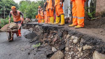 Petugas memindahkan batu dengan alat di Jalan Kesatrian X RT.12/3, Matraman, Jakarta Timur, Kamis (5/3). [Suara.com/Alfian Winanto]
