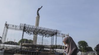 Warga melintas di depan pembangunan panggung musik di Lapangan Banteng, Jakarta, Jumat (6/3).  [ANTARA FOTO/Muhammad Adimaja]
