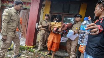 Tersangka Budi Rahmat menggendong korban saat reka ulang pembunuhan kepada anaknya sendiri pada rekontruksi di Cilembang, Kota Tasikmalaya, Jawa Barat, Kamis (12/3). [ANTARA FOTO/Adeng Bustomi]
