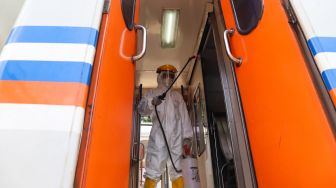 Petugas menyemprotkan cairan disinfektan di pintu gerbong kereta di Stasiun Pasar Senen, Jakarta, Minggu (15/3).[Suara.com/Alfian Winanto]