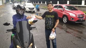 Aktivis membagikan sembako ke pengendara motor saat  menggelar #AksiPeduliLawanCorona didepan Kejagung, Jumat (20/3). [Suara.com/Oke Atmaja]
