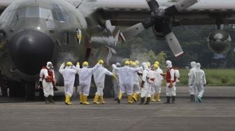 Petugas Palang Merah Indonesia (PMI) menyemprotkan cairan disinfektan kepada kru pesawat Hercules C-130 setibanya di Landasan Udara (Lanud) Halim Perdanakusuma, Jakarta, Senin (23/3). [Suara.com/Angga Budhiyanto