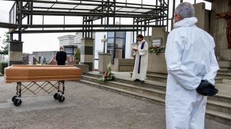 Seorang pendeta membacakan doa saat upacara pemakaman warga yang meninggal di pemakaman Grassobbio, Lombardia, Italia, Selasa (24/3).  [Piero CRUCIATTI / AFP]
