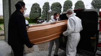 Pengurus jenazah memasukan peti mati warga yang meninggal karena virus Corona kedalam mobil jenazah di pemakaman Grassobbio, Lombardia, Italia, Selasa (24/3). [Piero CRUCIATTI / AFP]
