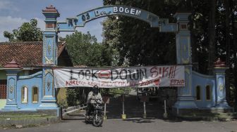 Warga melintas di depan spanduk penutupan jalan masuk Desa Bogem, Kalasan, Sleman, DI Yogyakarta, Senin (30/3). [ANTARA FOTO/Hendra Nurdiyansyah]