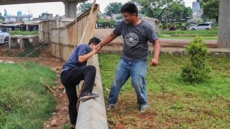 Warga saling membantu memanjat tembok karena akses jalan yang ditutup seng di RW 04 Cipinang Melayu, Jakarta Timur, Selasa (31/3). [Suara.com/Alfian Winanto]
