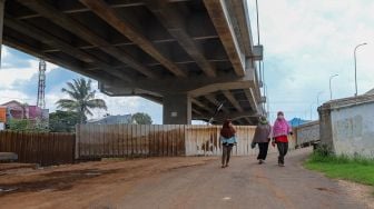 Warga melintasi jalan yang ditutup dengan seng untuk meminimalisir penyeberan  Corona di kawasan sekitar, Jakarta Timur, Selasa (31/3). [Suara.com/Alfian Winanto]