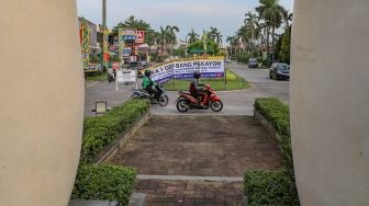 Pengendara motor melintas di depan spanduk pengumuman berisi karantina wilayah perumahan elit Kemang Pratama, Bekasi, Jawa Barat, Rabu (1/4). [Suara.com/Alfian Winanto]