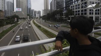 Seorang anak mengamati kendaraan yang melintas di Jalan Jendral Sudirman, Jakarta, Rabu (1/4). [Suara.com/Angga Budhiyanto]