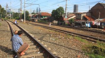 Warga bersama anaknya berjemur di rel kereta api di kawasan Menteng, Jakarta, Jumat (3/4). [Suara.com/Oke Atmaja]
