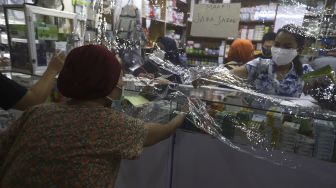 Pembeli beli obat dari balik plastik pembatas di salah satu apotek di kawasan Pasar Baru, Jakarta, Jumat (3/4). [Suara.com/Angga Budhiyanto]