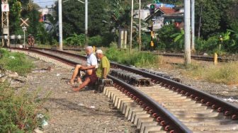 
Dua orang warga berjemur di rel kereta api di kawasan Menteng, Jakarta, Jumat (3/4). [Suara.com/Oke Atmaja]