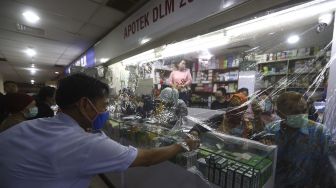 Pekerja melayani pembeli dari balik plastik pembatas di salah satu apotek di kawasan Pasar Baru, Jakarta, Jumat (3/4). [Suara.com/Angga Budhiyanto]