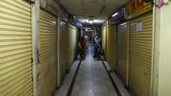 Pengunjung melintasi pertokoan yang tutup akibat merebaknya virus Corona di Pasar Jatinegara, Jakarta Timur, Sabtu (4/4). [Suara.com/Alfian Winanto]