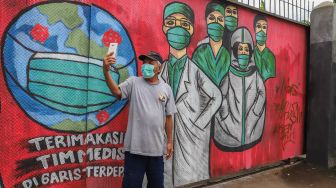 Warga berfoto selfie di depan mural bertemakan Virus Corona di Jalan Raya Bogor,  Depok, Jawa Barat, Senin (6/4). [Suara.com/Alfian Winanto]