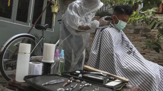 Seorang tukang cukur menggunakan Alat Pelindung Diri (APD) ketika memotong rambut di halaman rumah pelanggan di Pekanbaru, Riau, Kamis (9/4). [ANTARA FOTO/Rony Muharrman]