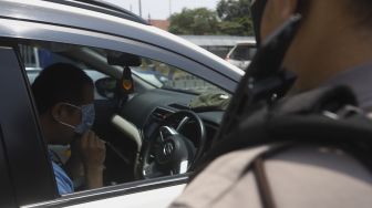 Polisi memeriksa pengendara mobil saat melaksanakan pengawasan dalam penerapan Pembatasan Sosial Berskala Besar (PSBB) di pintu tol Pasar Rebo 2, Jakarta, Jumat (10/4). [Suara.com/Angga Budhiyanto]